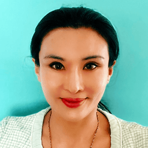 A woman with long dark hair, wearing a light green plaid jacket and necklace, smiles at the camera against a bright turquoise background.